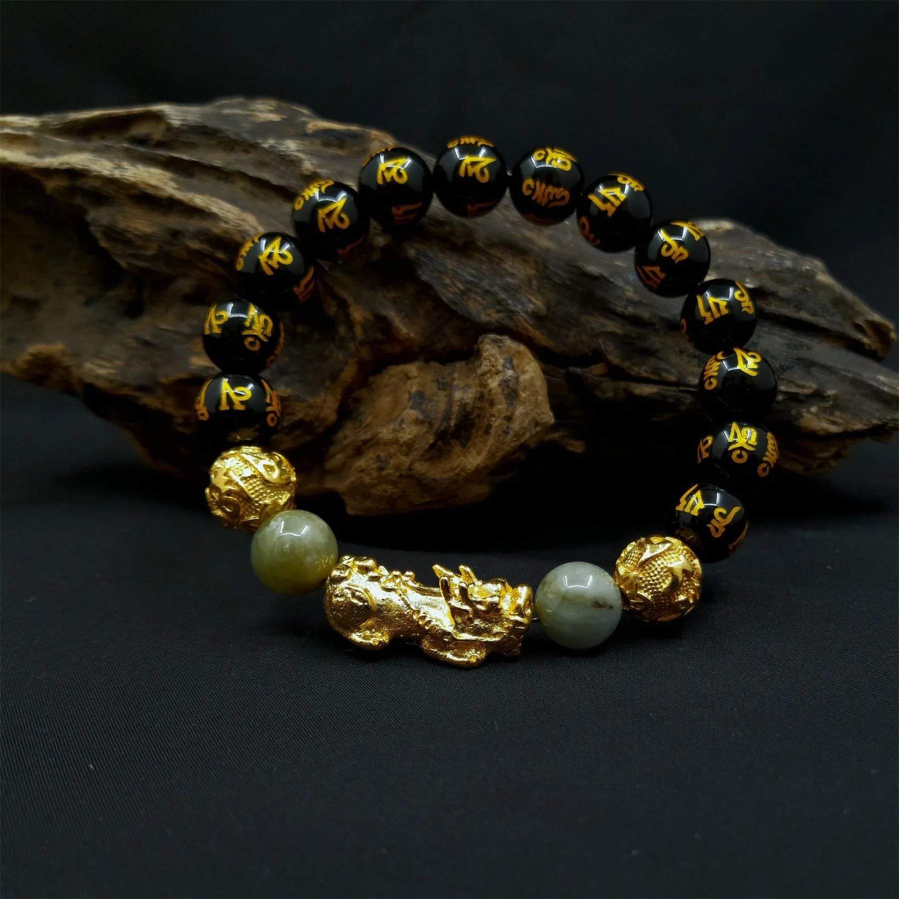 Black obsidian and jade feng shui bracelet with a gold prosperity detail on a dark styled surface