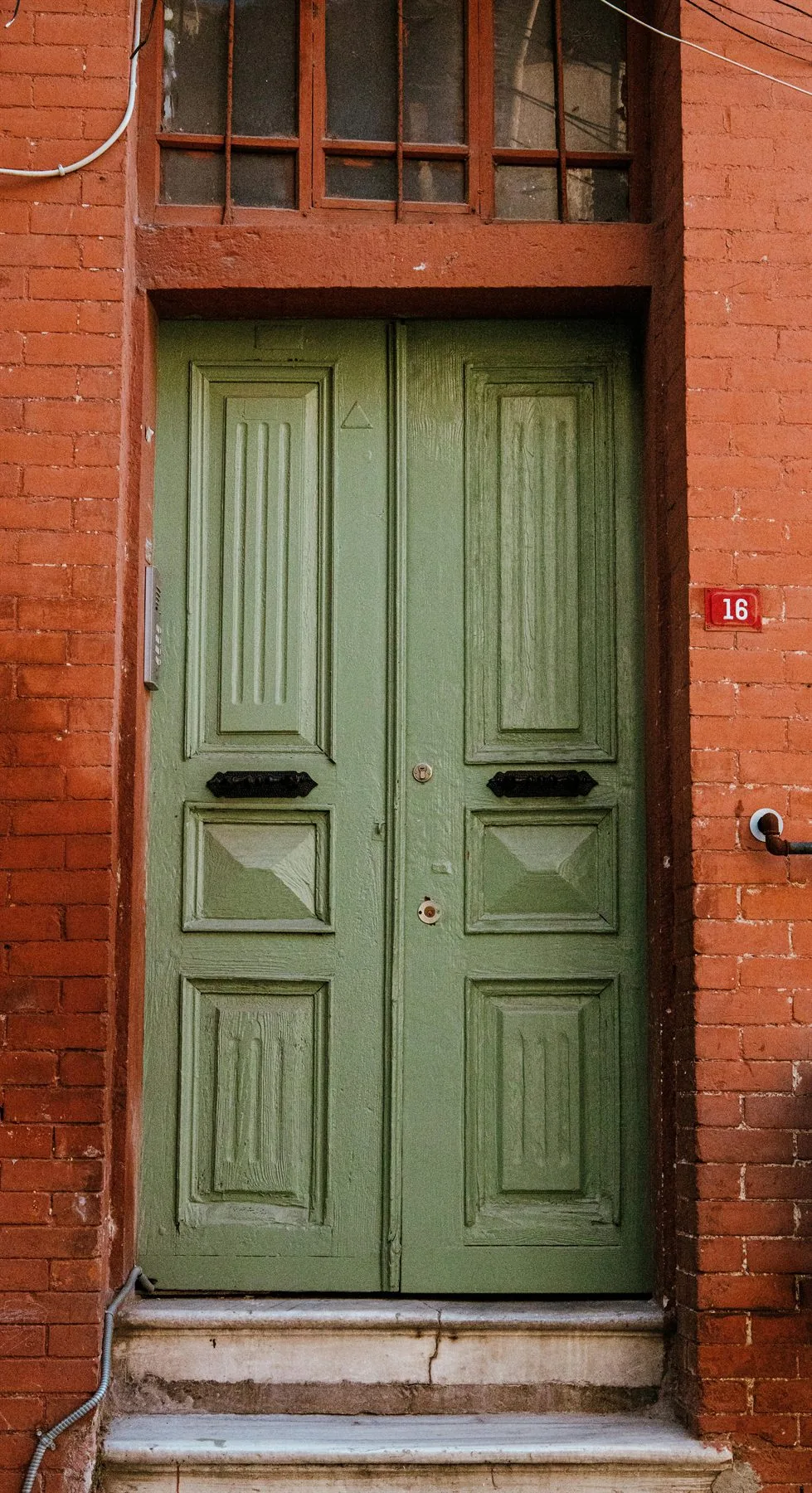 Weathered olive-green front door set into a brick exterior
