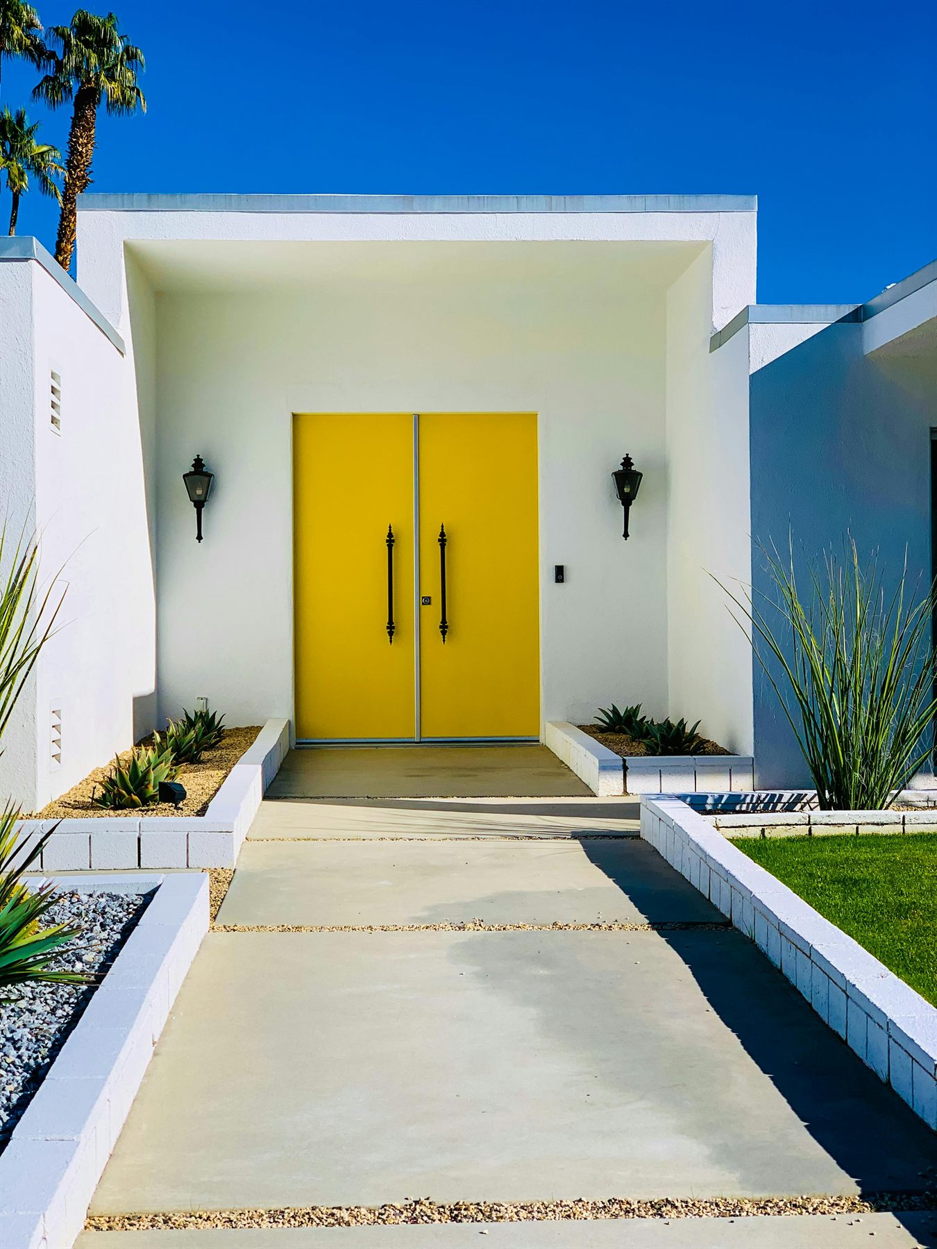 Modern white house with bold yellow front doors and symmetrical walkway