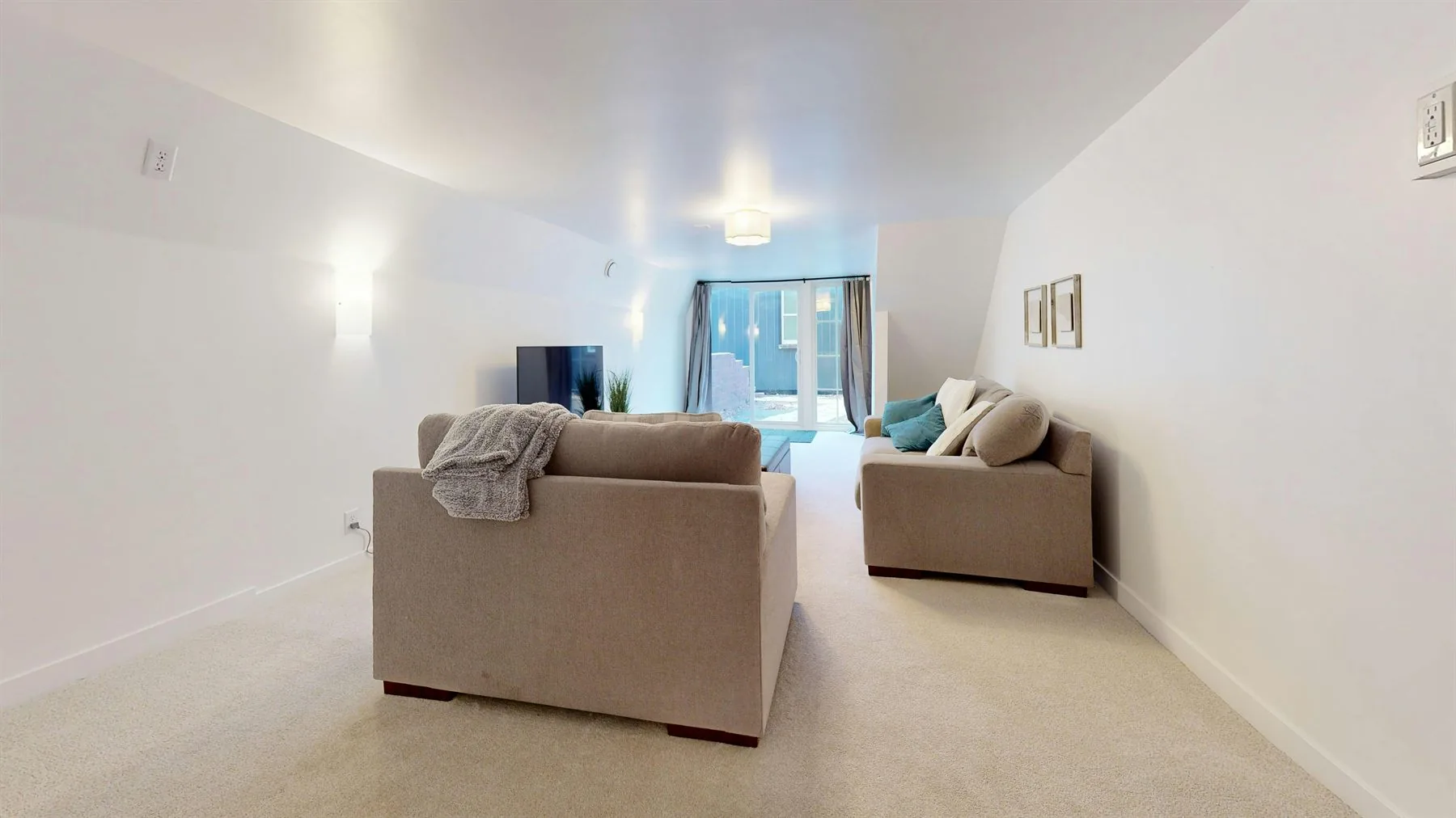 Long neutral room with beige seating, carpet, and softly lit white walls
