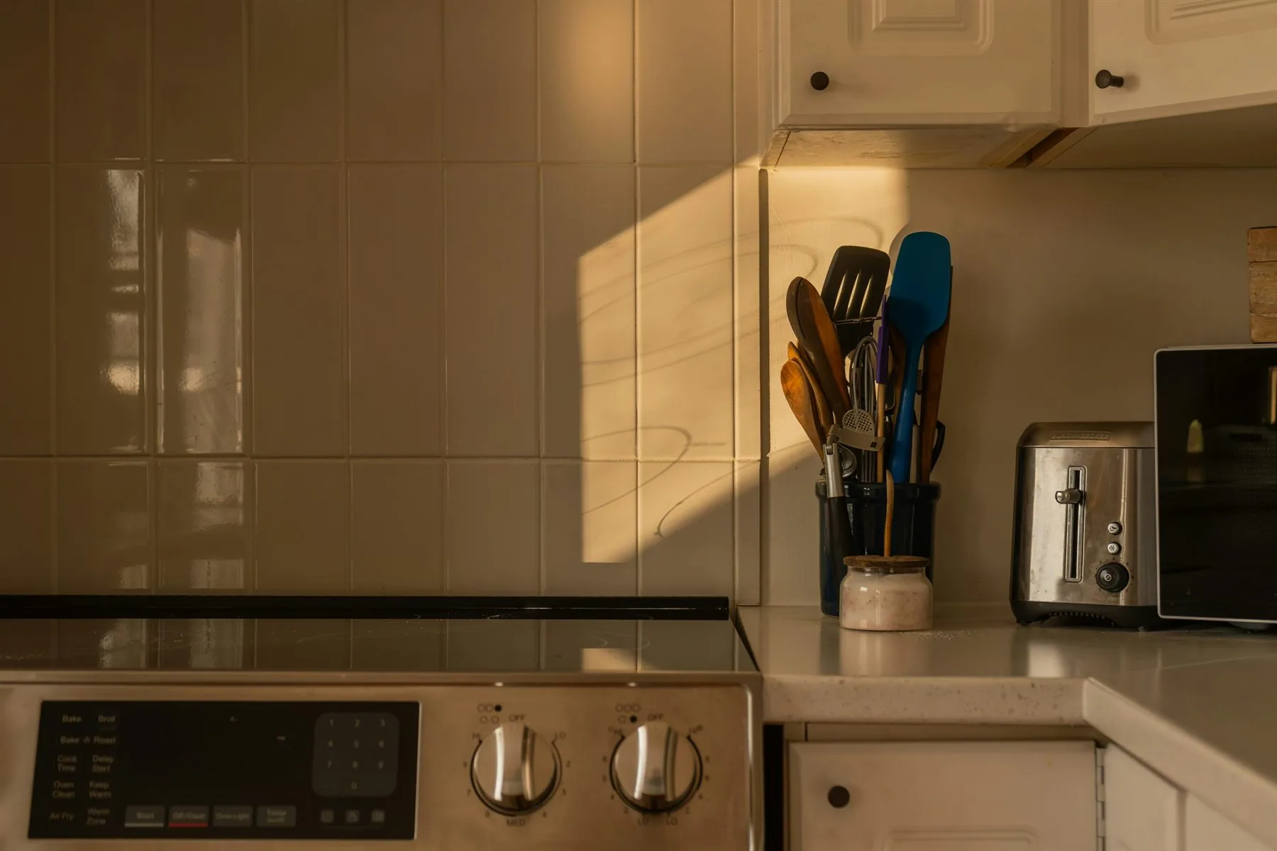 Kitchen counter at golden hour with cream tile, toaster, and utensils in soft warm light