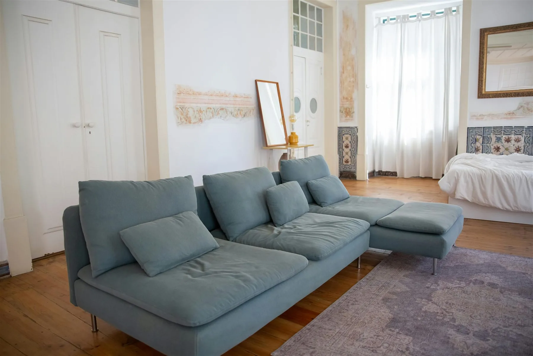 Living room with dusty blue-green sectional, pale rug, and wood floor
