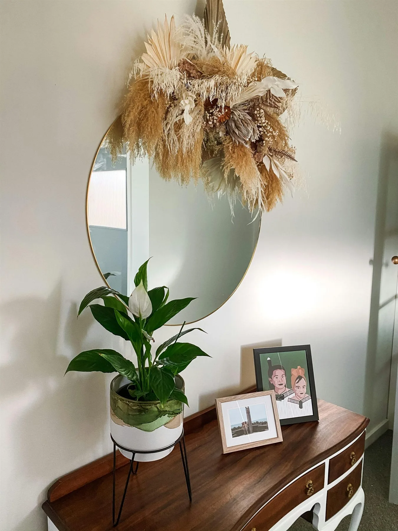 Round mirror above a console with plant, photos, and a calm entry arrangement