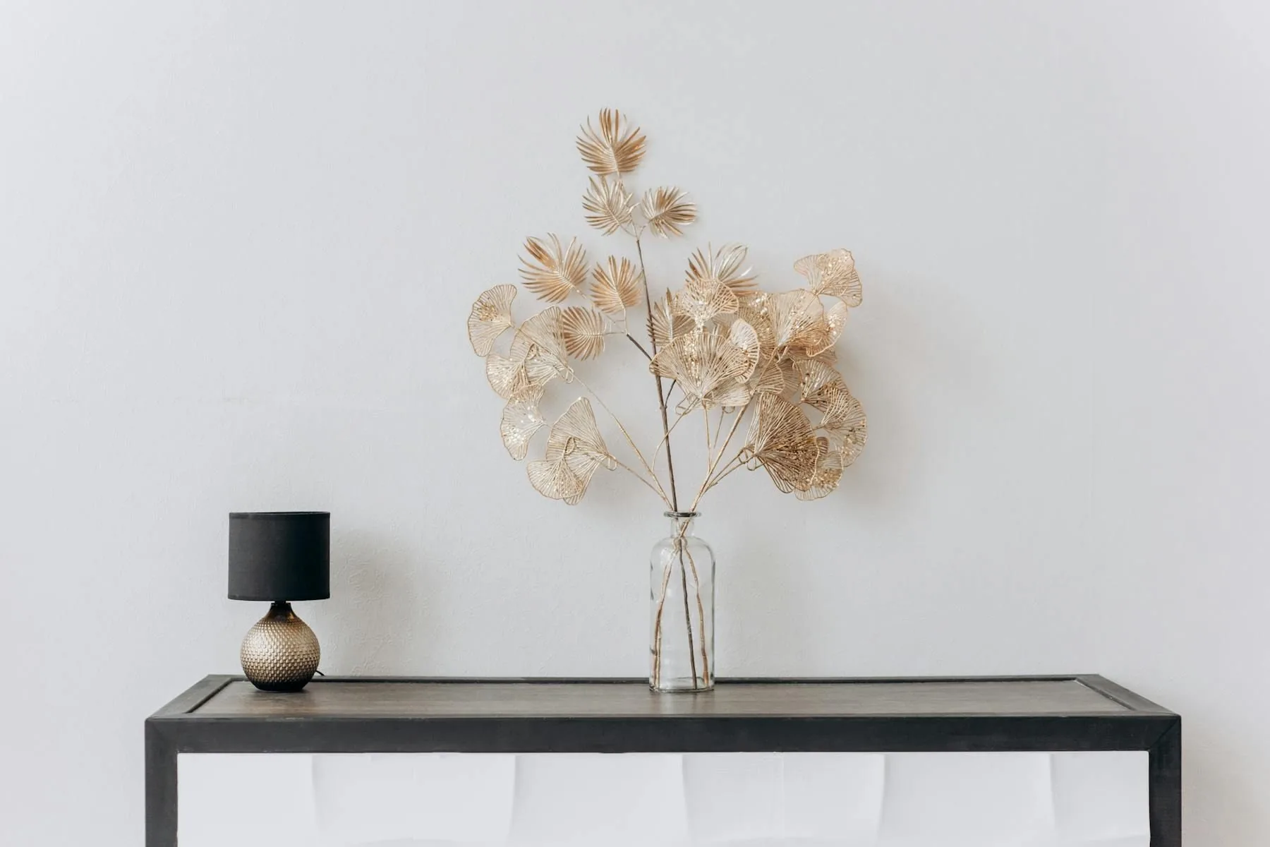 Minimal console with a small lamp and airy gold-toned botanical arrangement