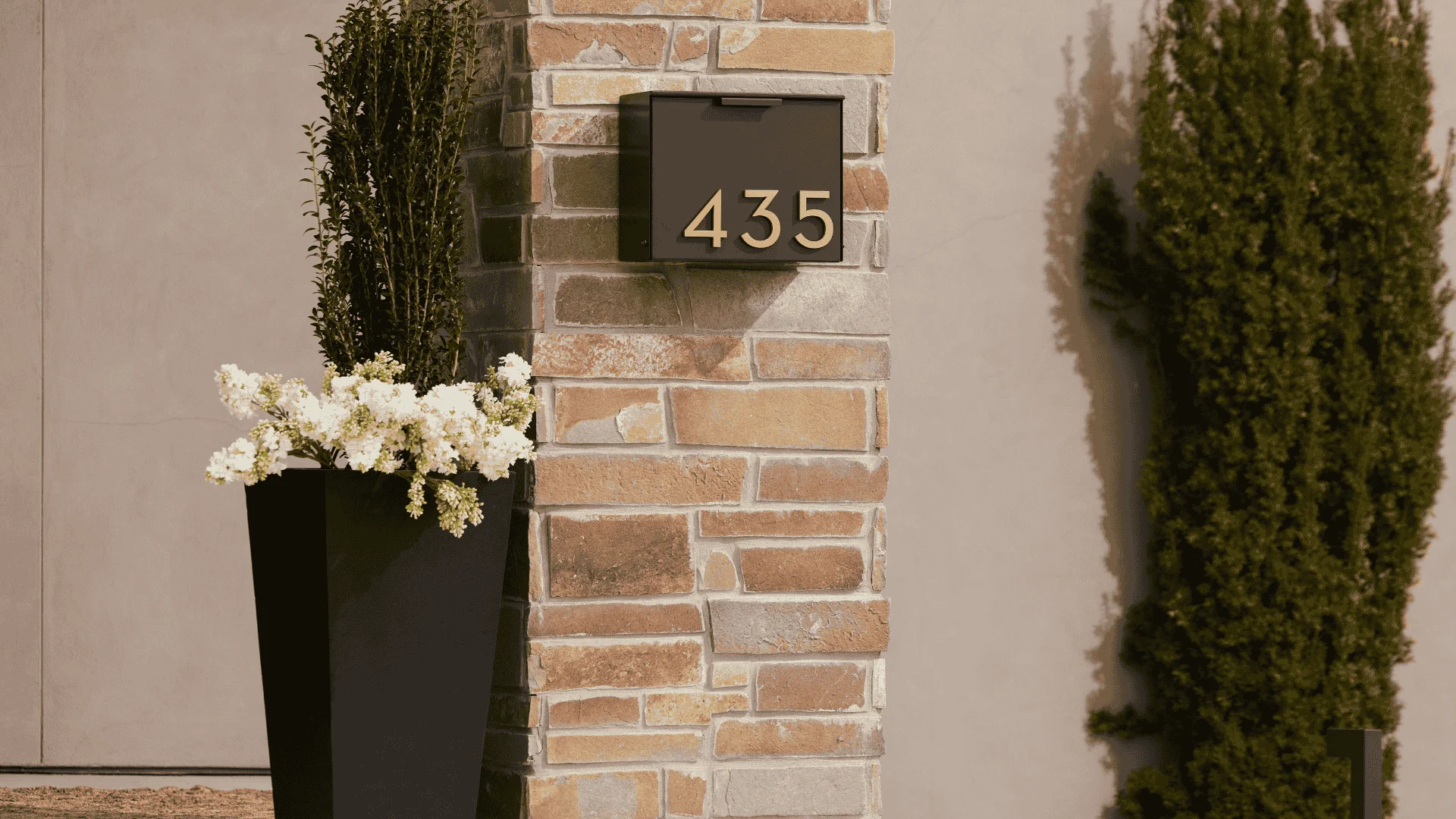 Stone entry column with a clean house number plaque and a structured planter beside it