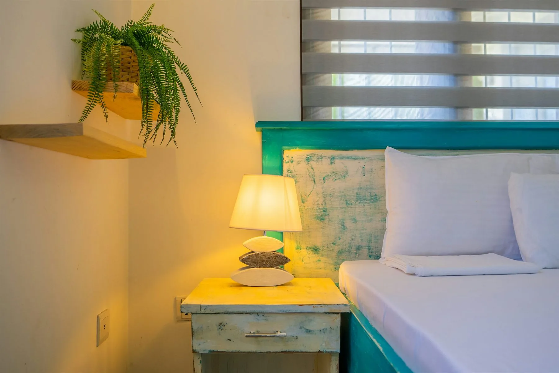 Bedroom close-up with a teal headboard, warm lamp, and shelf styling