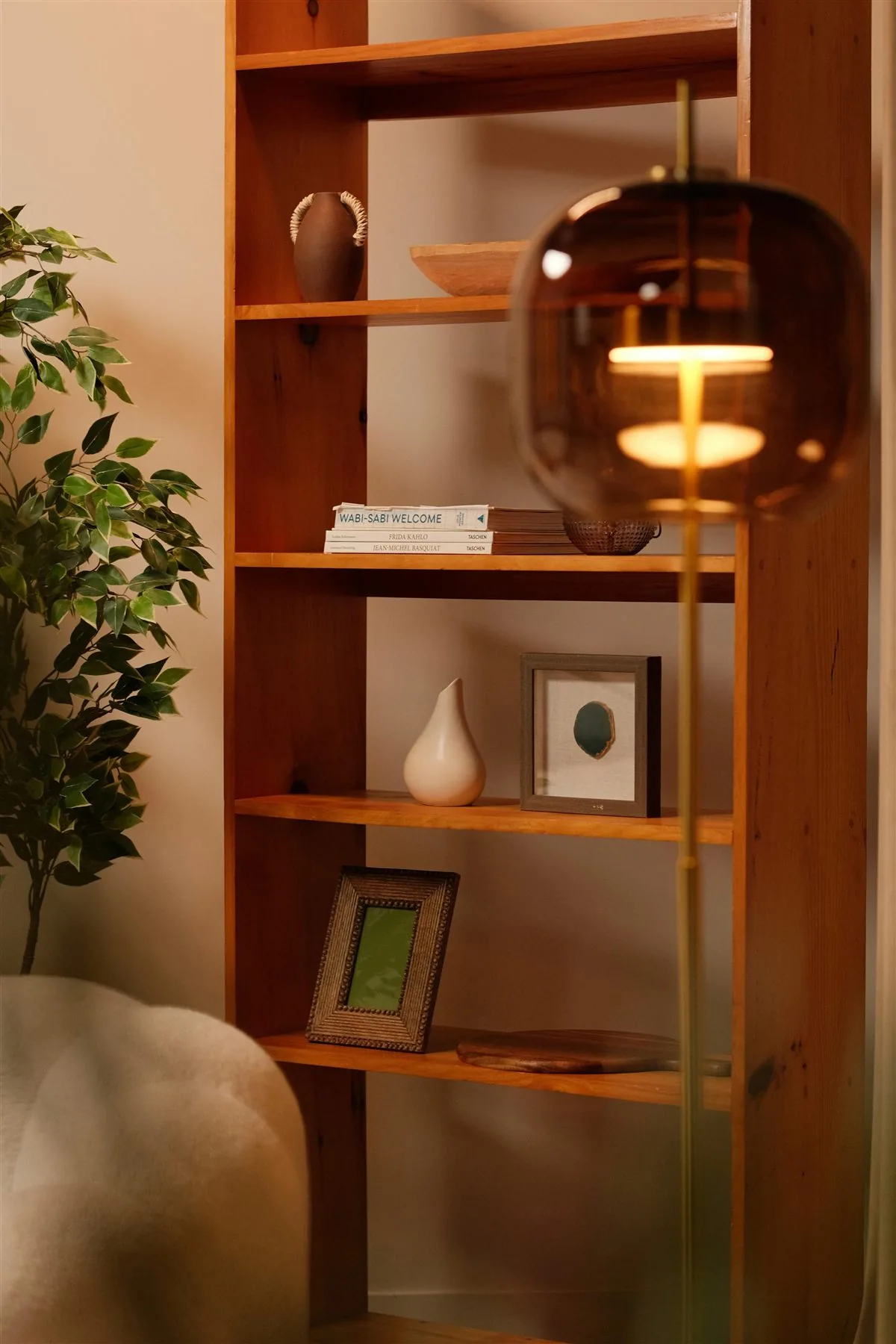 Warm wooden shelf with a glowing lamp, framed art, books, and a plant
