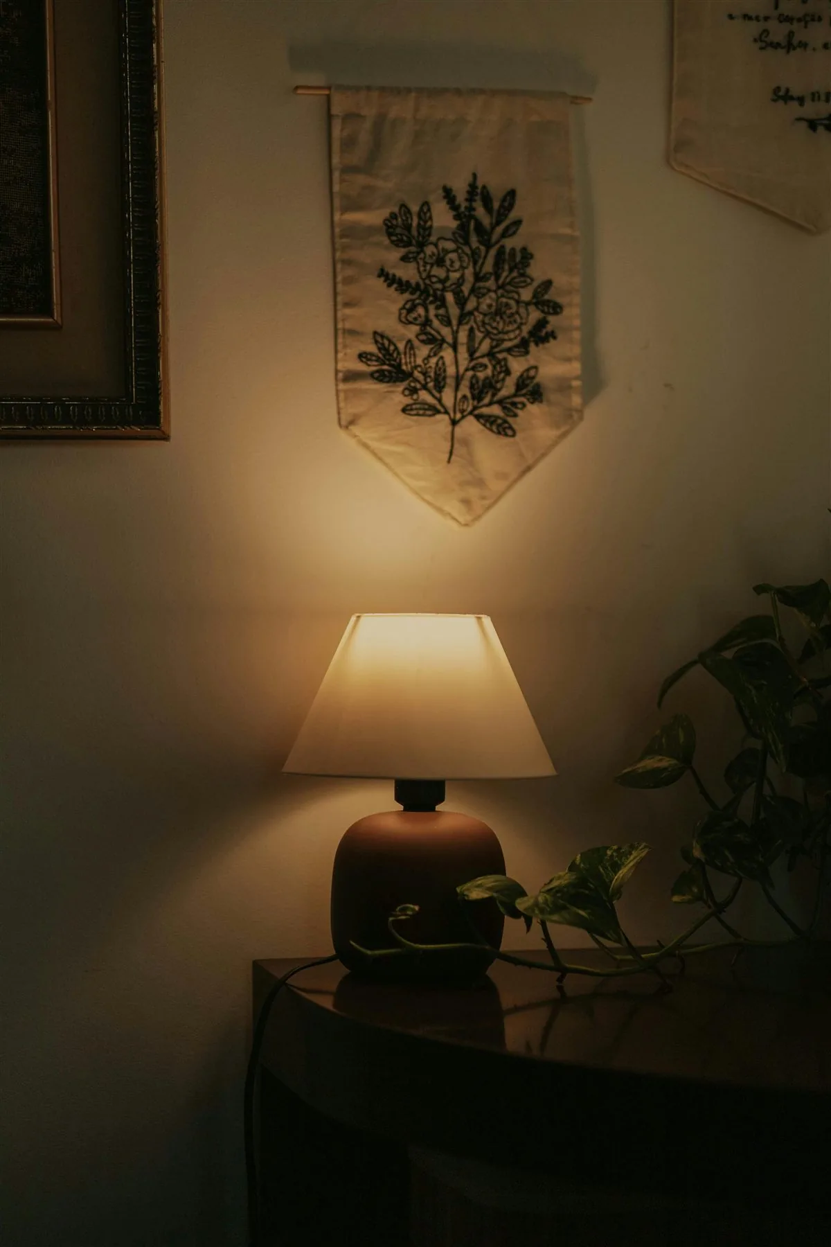 Warm lamp on a table beneath textile wall art with a plant nearby